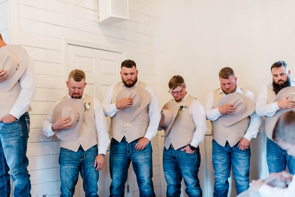 groomsmen holding cowboy hats while praying